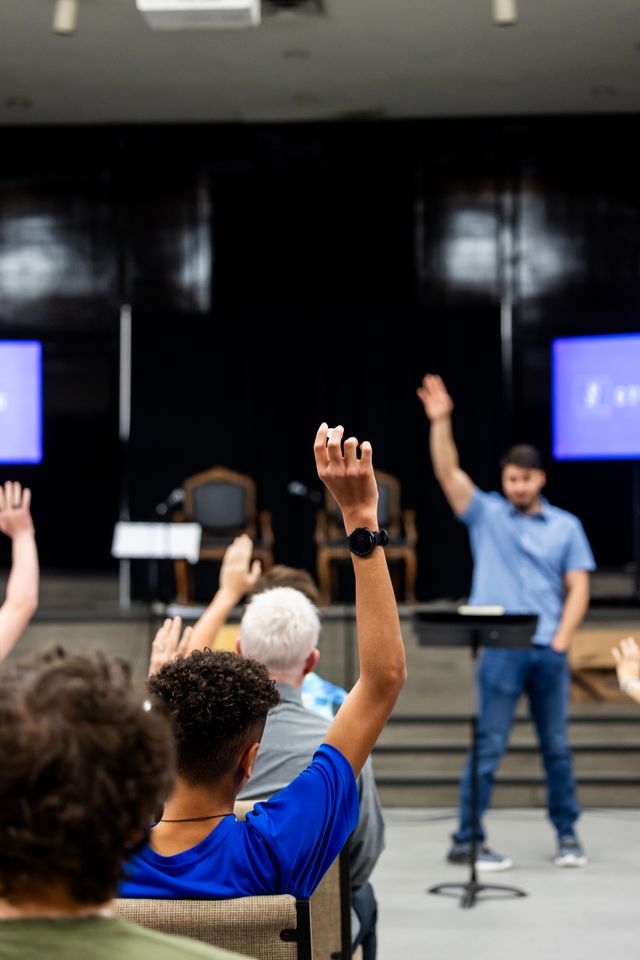 Instructor engaging with audience in an indoor classroom setting, hands raised for questions.